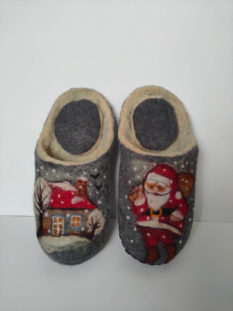 May include: A pair of gray wool slippers with a winter scene design. One slipper features a house with a red roof and a snowy landscape. The other slipper features Santa Claus with a bag of gifts.