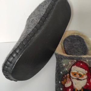 May include: Gray felt slippers with a black leather trim and a Santa Claus design on the front. The slippers have a black rubber sole.