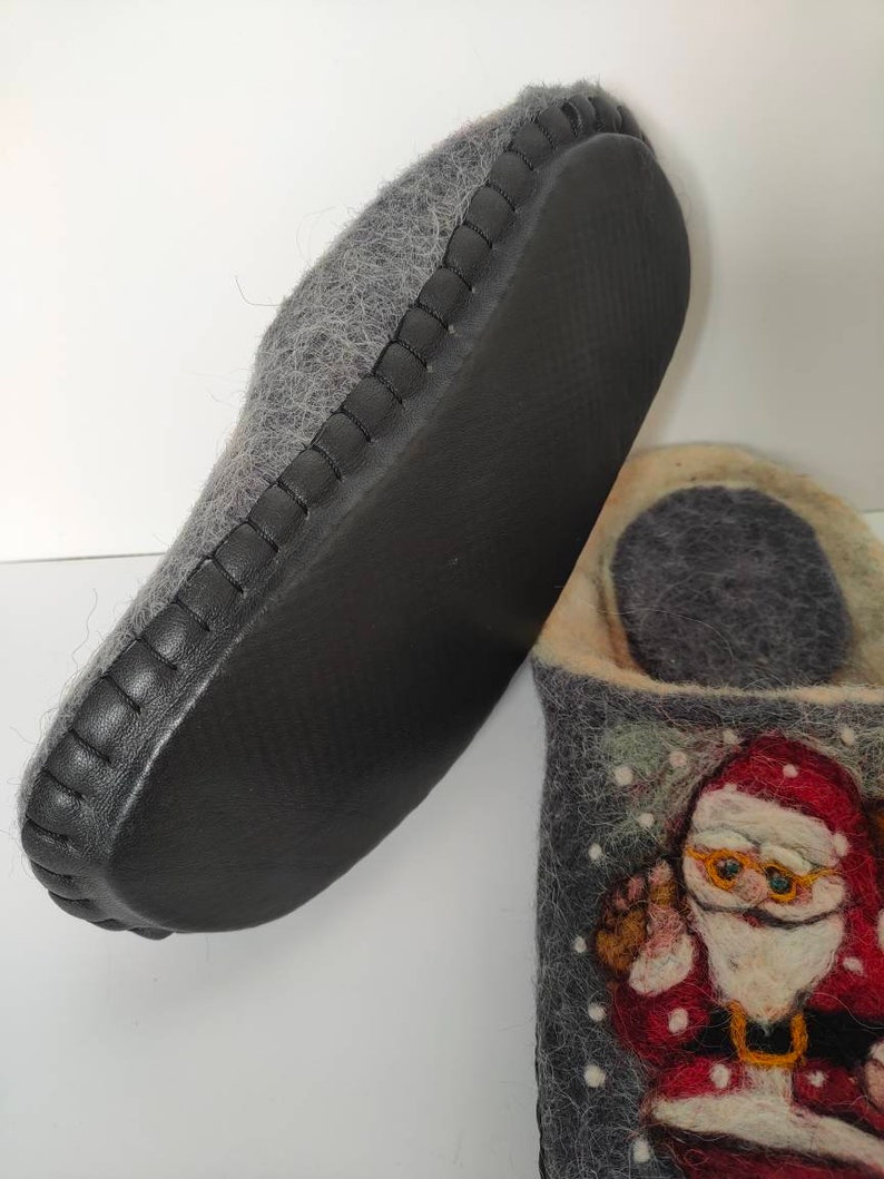May include: Gray felt slippers with a black leather trim and a Santa Claus design on the front. The slippers have a black rubber sole.