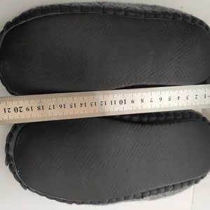 May include: A pair of gray fuzzy slippers with black rubber soles. The soles have a textured pattern and are measured with a ruler.