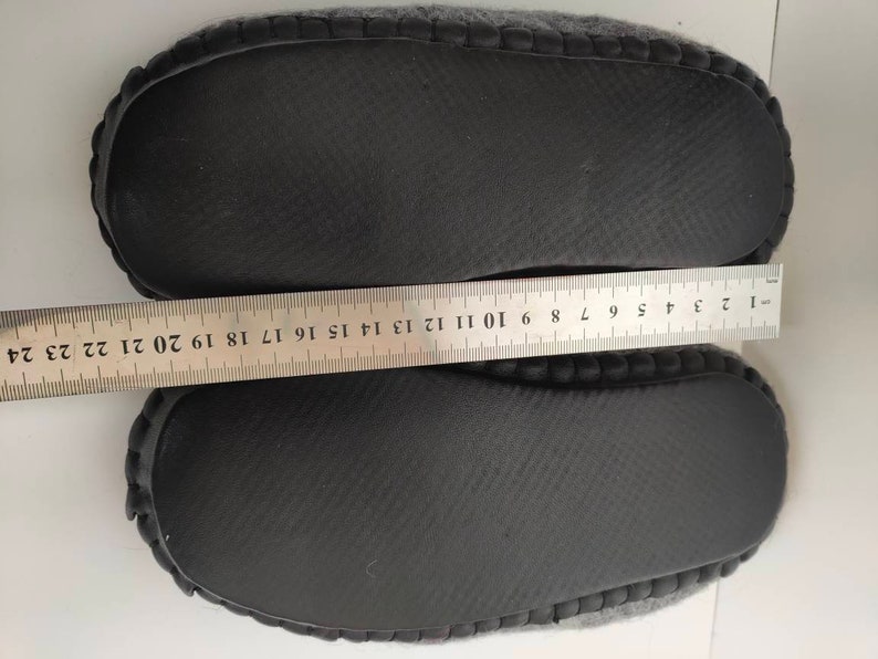 May include: A pair of gray fuzzy slippers with black rubber soles. The soles have a textured pattern and are measured with a ruler.