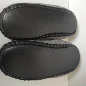May include: A pair of gray wool slippers with black rubber soles. The soles have a textured pattern.