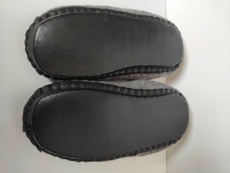 May include: A pair of gray wool slippers with black rubber soles. The soles have a textured pattern.
