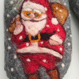 May include: A gray felt slipper with a red and white Santa Claus design. The Santa Claus is wearing a red suit with white trim, a white beard, and a black belt. He is holding a brown bag on his back.