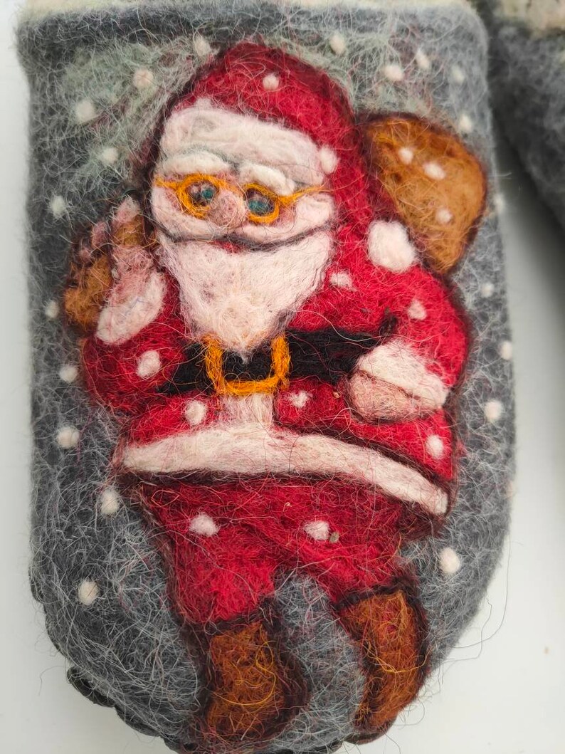 May include: A gray felt slipper with a red and white Santa Claus design. The Santa Claus is wearing a red suit with white trim, a white beard, and a black belt. He is holding a brown bag on his back.
