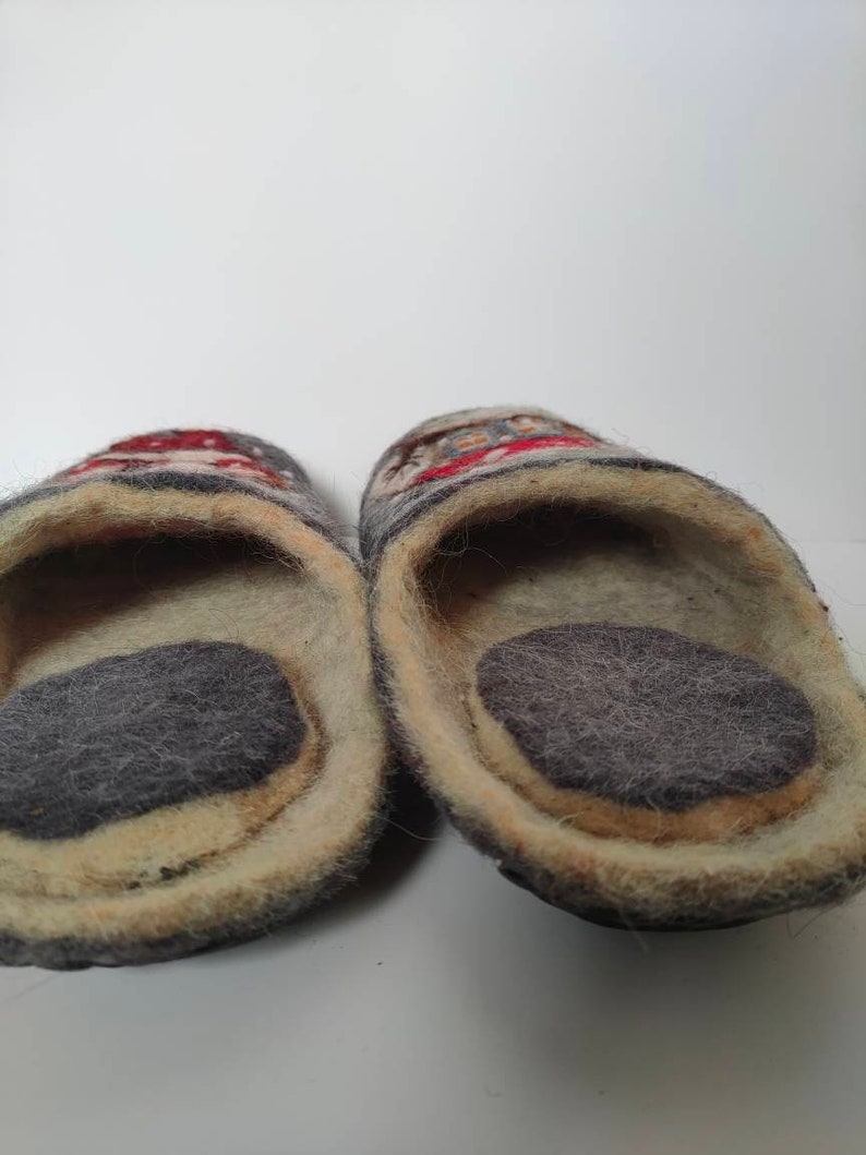 May include: A pair of gray wool slippers with a colorful design. The slippers have a soft, fuzzy lining and a gray felt sole.