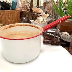 Puede incluir: Cacerola de esmalte blanco con borde rojo y asa roja. La cacerola está vacía y tiene algunas manchas marrones en el interior.