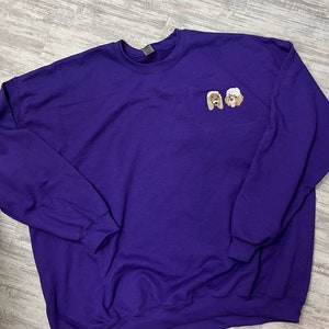 K&ouml;nnte beinhalten: Ein lilafarbener Pullover mit zwei gestickten Bildern von Hunden auf der Vorderseite. Die Hunde sind ein brauner und wei&szlig;er Pudel.