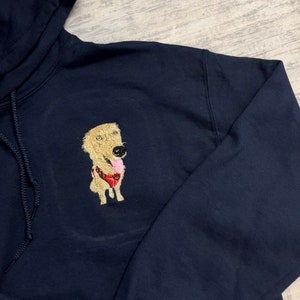 K&ouml;nnte beinhalten: Ein marineblauer Kapuzenpullover mit einem gestickten Bild eines Golden Retriever-Hundes, der einen roten Ball im Maul h&auml;lt.