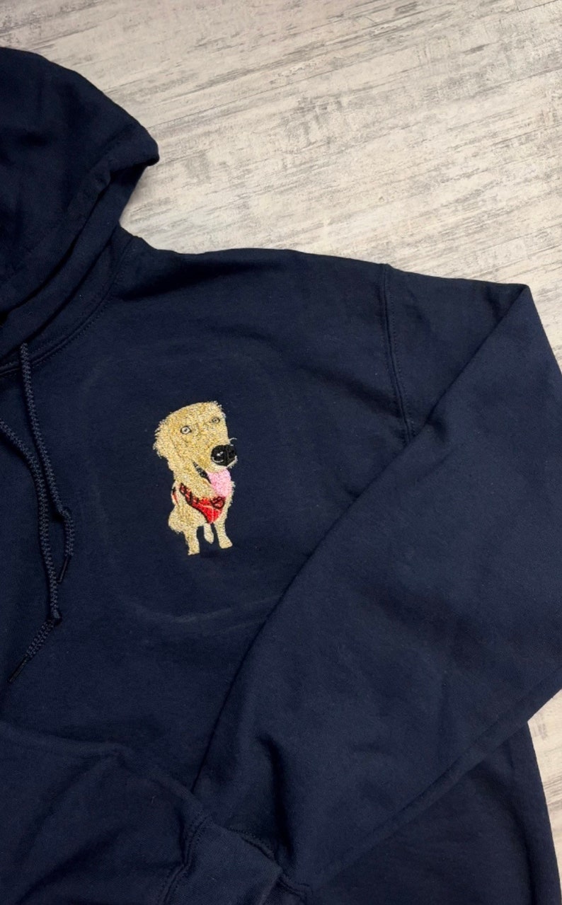 K&ouml;nnte beinhalten: Ein marineblauer Kapuzenpullover mit einem gestickten Bild eines Golden Retriever-Hundes, der einen roten Ball im Maul h&auml;lt.