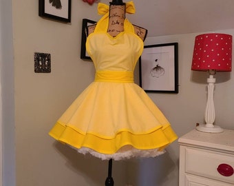 May include: A yellow halter dress with a white gingham pattern, a yellow waistband, and a layered skirt with a white trim. The dress is displayed on a mannequin with a black stand. A yellow bow is at the top of the dress.