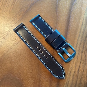 May include: Two-piece watch strap in dark brown leather with white stitching. The strap has a silver-colored buckle and five adjustment holes. The leather has a smooth finish.