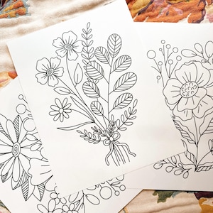 May include: Three black and white line drawings of floral bouquets. The bouquets are made up of various flowers and leaves. The drawings are on white paper.