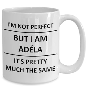 Peut inclure: Une tasse à café en céramique blanche avec du texte noir qui dit "Je ne suis pas parfaite mais je suis Adéla c'est à peu près la même chose."