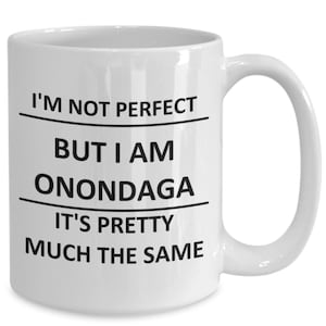 以下が含まれることがあります： 白いセラミック製のコーヒーカップで、黒い文字で「完璧ではないけど、私はオノンダーガ、ほぼ同じだよ。」と書かれています。