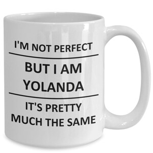 May include: White ceramic mug with a curved handle. The mug features the text "I'M NOT PERFECT BUT I AM YOLANDA IT'S PRETTY MUCH THE SAME" in black, divided by horizontal lines. A humorous gift idea.