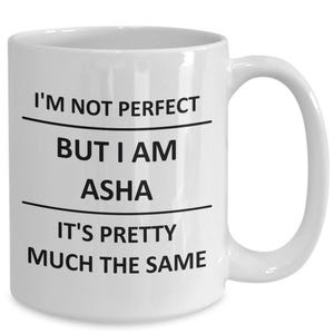 May include: White ceramic mug with a curved handle. The mug features black text that reads "I'M NOT PERFECT BUT I AM ASHA IT'S PRETTY MUCH THE SAME". The mug is designed for beverages.
