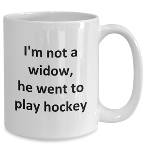 May include: White ceramic coffee mug with black text that reads "I'm not a widow, he went to play hockey".