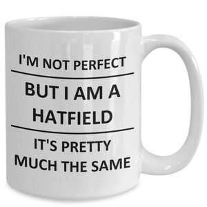 May include: White ceramic coffee mug with black text that reads "I'm not perfect but I am a Hatfield it's pretty much the same".