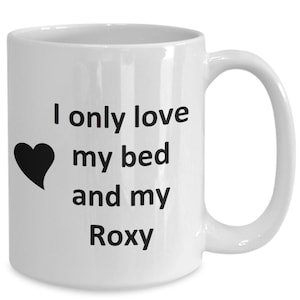 May include: White ceramic coffee mug with black text that reads "I only love my bed and my Roxy". A black heart is to the left of the text.