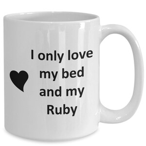May include: White ceramic coffee mug with black text that reads "I only love my bed and my Ruby". A black heart is to the left of the text.