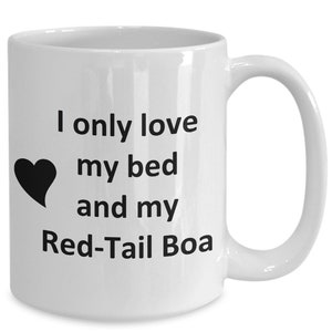 May include: White ceramic coffee mug with black text that reads "I only love my bed and my Red-Tail Boa". A black heart is to the left of the text.