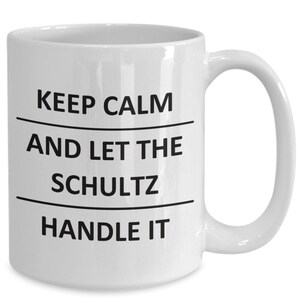 May include: White ceramic coffee mug with black text that reads "Keep Calm and Let the Schultz Handle It."