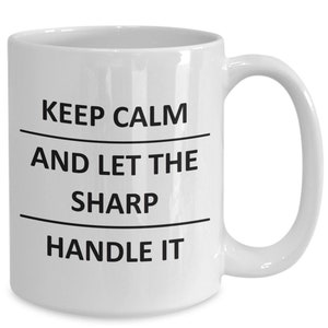 May include: White ceramic coffee mug with black text that reads "Keep Calm and Let the Sharp Handle It".