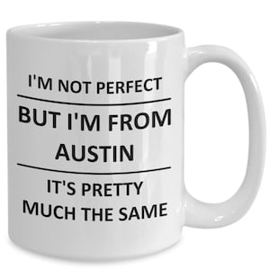 May include: White ceramic coffee mug with black text that reads "I'm not perfect but I'm from Austin. It's pretty much the same."