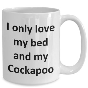 May include: White ceramic mug with a curved handle. The mug features the text "I only love my bed and my Cockapoo" in black, bold font. The mug is designed for hot beverages and is suitable for home or office use.
