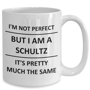 May include: White ceramic coffee mug with black text that reads "I'm not perfect but I am a Schultz it's pretty much the same."