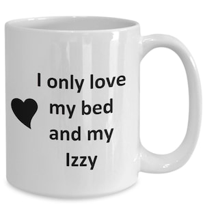 May include: White ceramic coffee mug with a black heart and the text "I only love my bed and my Izzy" printed on it.