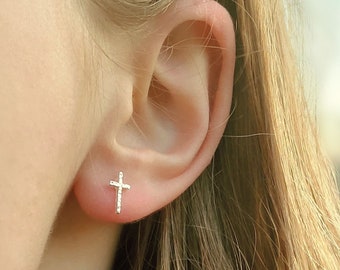 May include: A close-up of a person's ear with a small, silver cross earring. The earring is a simple, minimalist design.