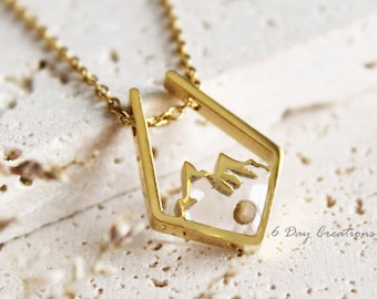 Puede incluir: Collar de oro con un colgante geométrico que presenta una silueta de montaña en su interior. El colgante está abierto en la parte superior e inferior, creando un efecto de marco. El collar está sobre una superficie blanca texturizada.