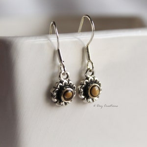 May include: A pair of silver dangle earrings with a small brown stone in the centre of each earring. The earrings are in the shape of a flower.