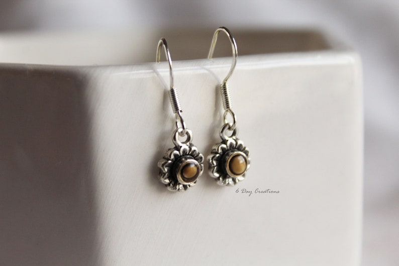 May include: A pair of silver dangle earrings with a small brown stone in the centre of each earring. The earrings are in the shape of a flower.