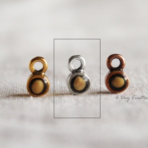 Pu&ograve; includere: Tre piccoli ciondoli in metallo con un centro rotondo giallo e un contorno nero. I ciondoli sono in oro, argento e rame.