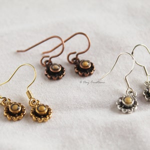 May include: Three pairs of dangle earrings with a small round stone in the centre of a flower design. The earrings are gold, silver, and copper.