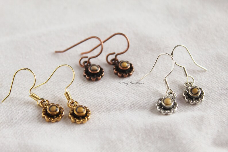 May include: Three pairs of dangle earrings with a small round stone in the centre of a flower design. The earrings are gold, silver, and copper.