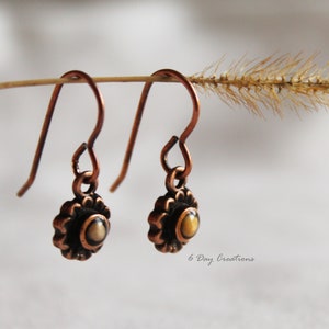 May include: A pair of copper dangle earrings with a small, round, yellow and brown stone set in a copper flower design.