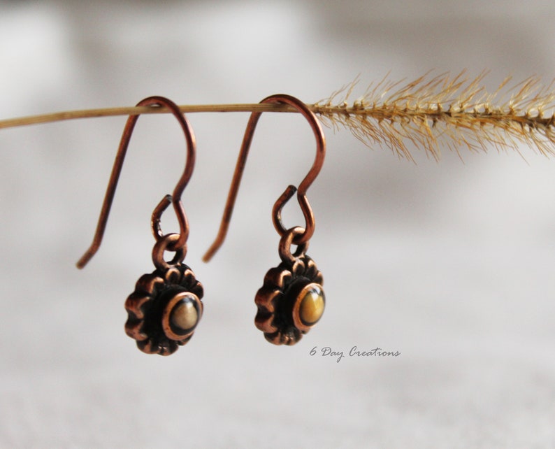 May include: A pair of copper dangle earrings with a small, round, yellow and brown stone set in a copper flower design.