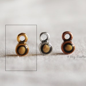 Pu&ograve; includere: Tre piccoli ciondoli in metallo con un anello in cima e un centro rotondo color crema. I ciondoli sono dorati, argentati e color rame.