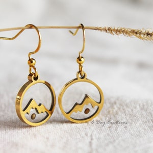 May include: Gold earrings with a clear glass circle containing a silhouette of a mountain range. The earrings have a simple hook fastening.