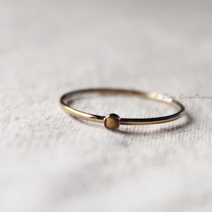 K&ouml;nnte beinhalten: Ein schlichter Goldring mit einem kleinen, runden, cremefarbenen Stein.