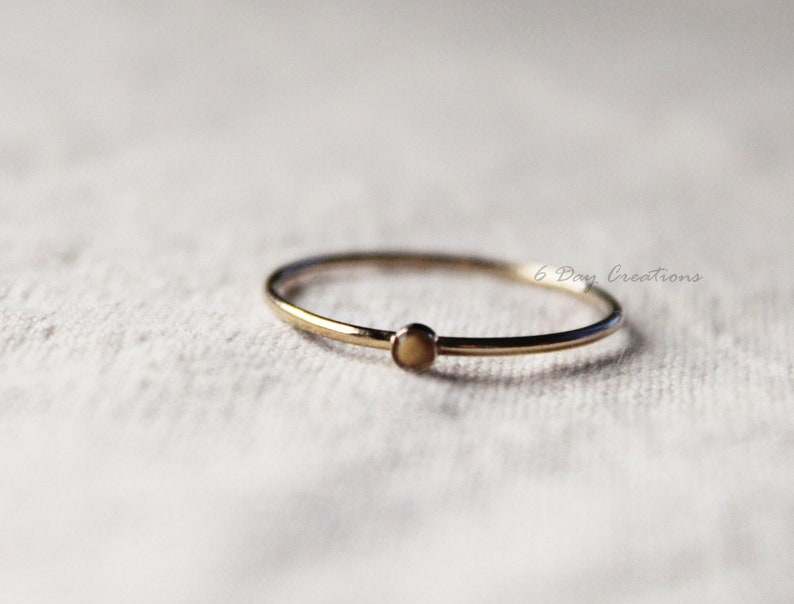 K&ouml;nnte beinhalten: Ein schlichter Goldring mit einem kleinen, runden, cremefarbenen Stein.