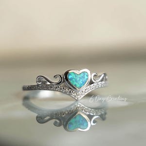 Op de afbeelding: Zilveren ring met een hartvormige, blauwgroene opaalsteen. De ring heeft een kroonontwerp met kleine, heldere stenen en decoratieve krullen. De tekst "6 Day Creations" is zichtbaar.