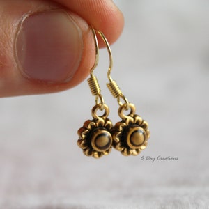 May include: Gold dangle earrings with a small flower design and a brown centre. The earrings have a spring-loaded hook closure.