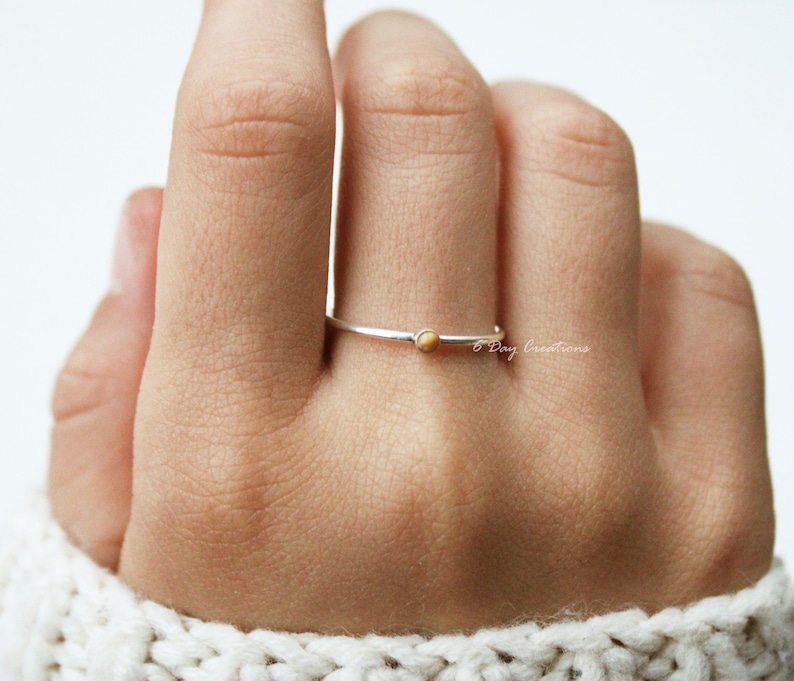 K&ouml;nnte beinhalten: Ein schlichter Silberring mit einem kleinen, runden, hellbraunen Edelstein. Der Ring wird an einem Finger getragen.