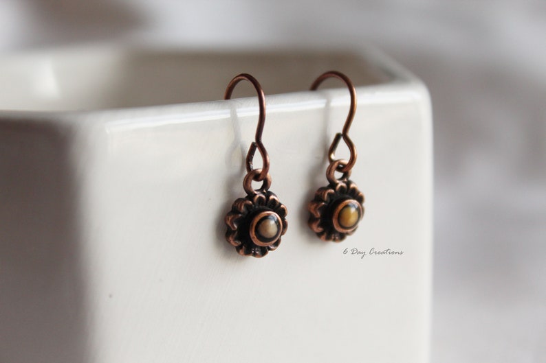 May include: A pair of copper earrings with a small, round, white and brown stone in the centre of each earring.