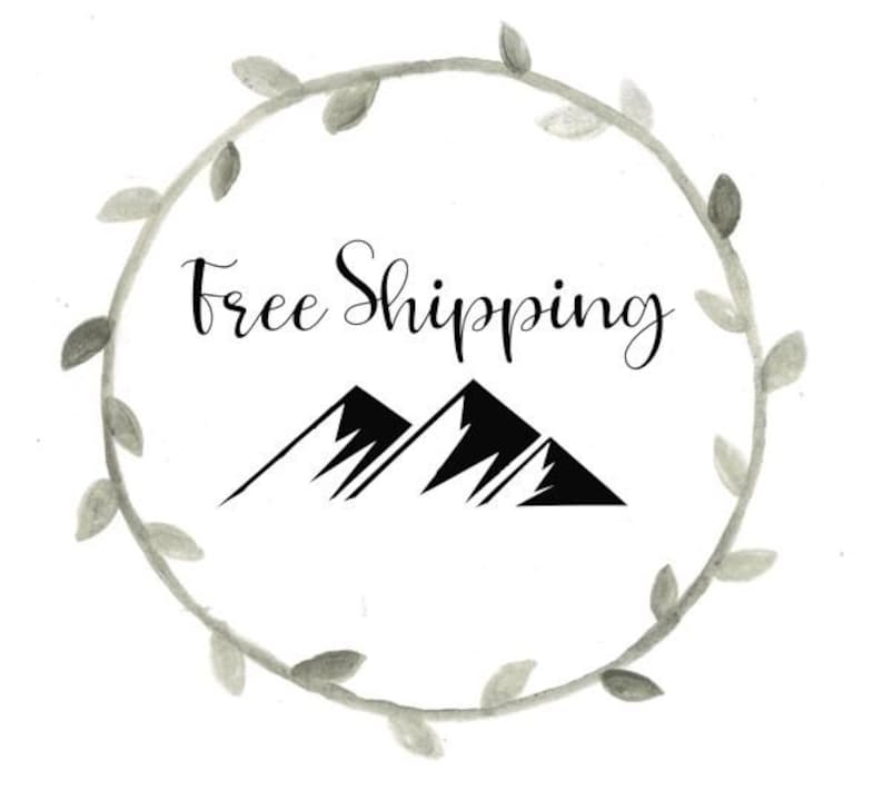 May include: A black and white illustration of two mountains with the text "Free Shipping" in a grey watercolour wreath.